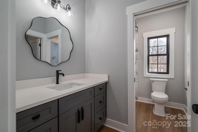 bathroom with toilet, wood finished floors, vanity, and baseboards