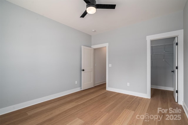 unfurnished bedroom featuring a closet, a spacious closet, light wood-style floors, a ceiling fan, and baseboards