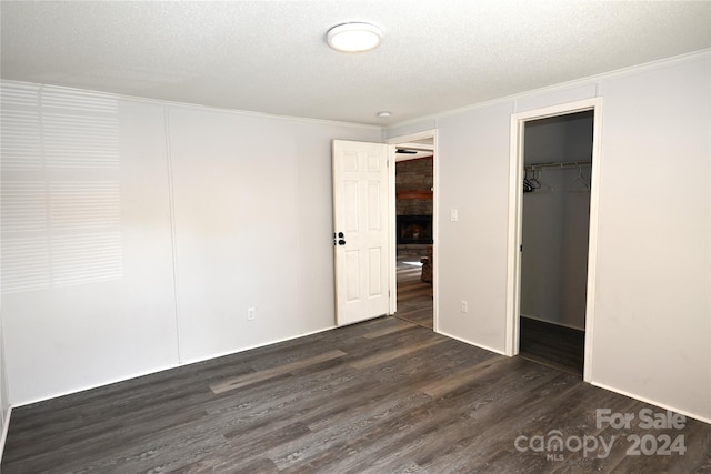 unfurnished bedroom featuring a closet, a textured ceiling, dark hardwood / wood-style flooring, and a spacious closet