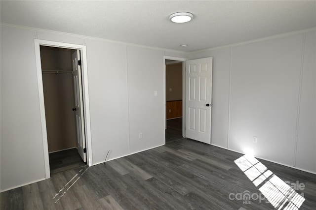 unfurnished bedroom with a walk in closet, a textured ceiling, a closet, crown molding, and dark hardwood / wood-style floors