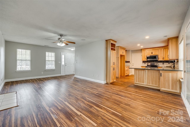 kitchen featuring tasteful backsplash, appliances with stainless steel finishes, light brown cabinetry, dark wood-type flooring, and kitchen peninsula