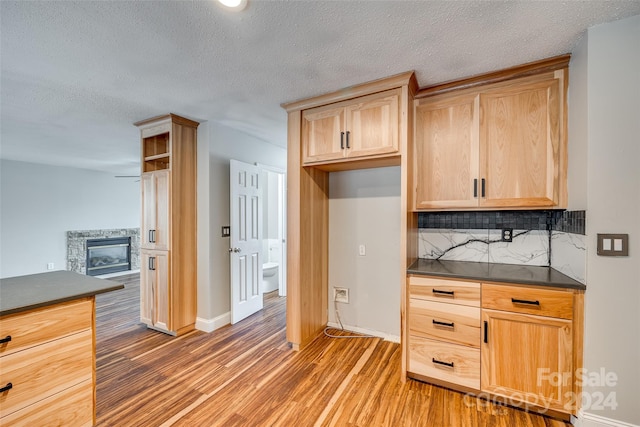 kitchen with hardwood / wood-style flooring, tasteful backsplash, light brown cabinets, a textured ceiling, and a stone fireplace