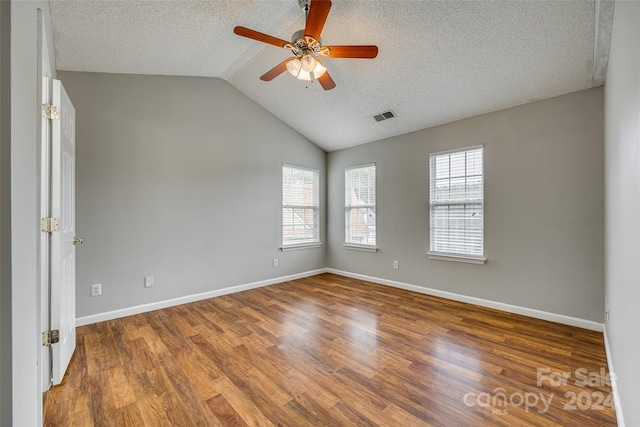 unfurnished room with hardwood / wood-style flooring, a textured ceiling, lofted ceiling, and a healthy amount of sunlight