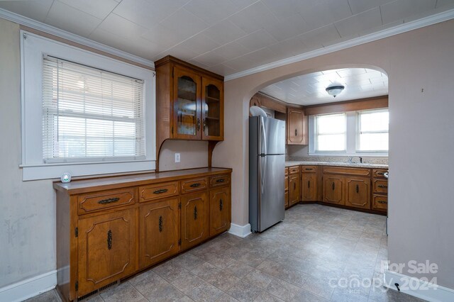 24947 Nc-24/27 Hwy, Albemarle, NC 28001 - kitchen featuring freestanding refrigerator, brown cabinetry, crown molding, arched walkways, and glass insert cabinets