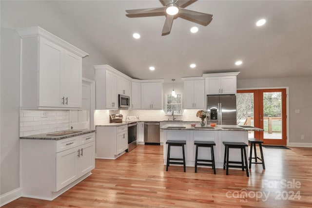 kitchen featuring white cabinets, light hardwood / wood-style floors, a kitchen island, a kitchen bar, and stainless steel appliances