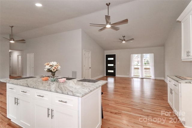 kitchen featuring vaulted ceiling, a kitchen island, light stone countertops, light hardwood / wood-style floors, and white cabinetry