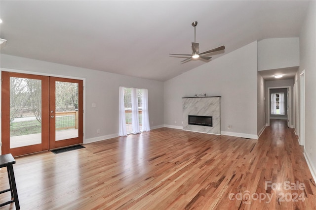 unfurnished living room featuring high vaulted ceiling, french doors, light hardwood / wood-style flooring, ceiling fan, and a fireplace