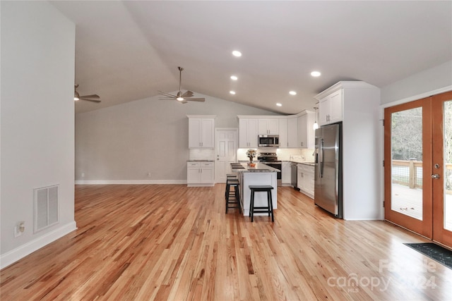 kitchen with stainless steel appliances, a kitchen island, light hardwood / wood-style floors, a breakfast bar, and white cabinets