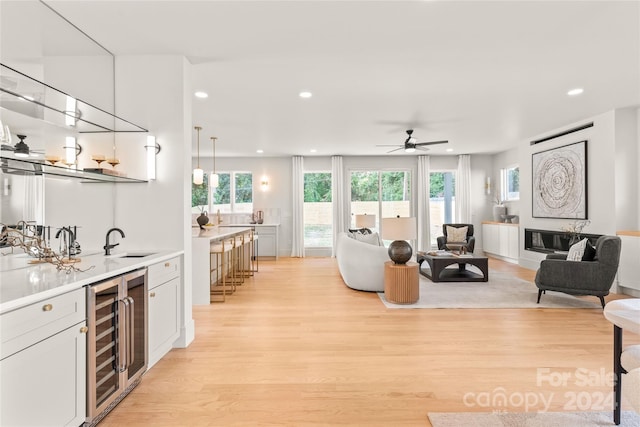 living room featuring beverage cooler, indoor wet bar, ceiling fan, and light hardwood / wood-style floors