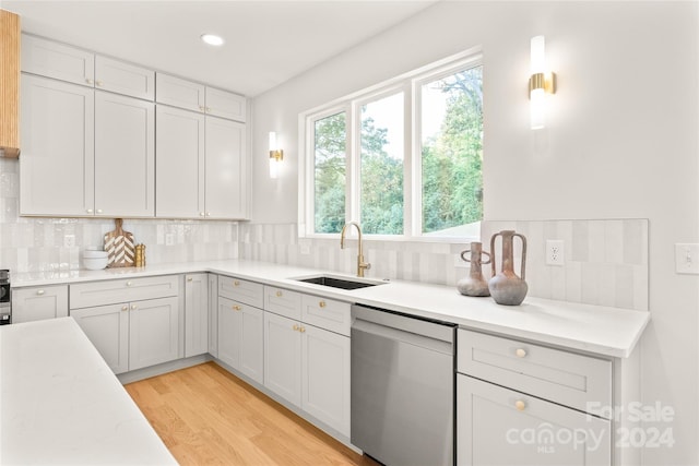 kitchen with tasteful backsplash, stainless steel dishwasher, sink, and light hardwood / wood-style flooring