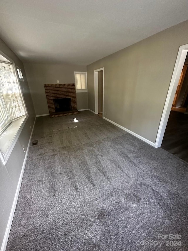 unfurnished living room featuring a brick fireplace and dark colored carpet