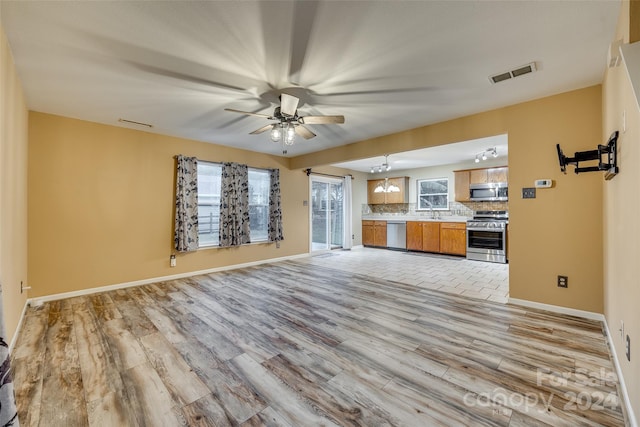 unfurnished living room with ceiling fan with notable chandelier and light wood-type flooring