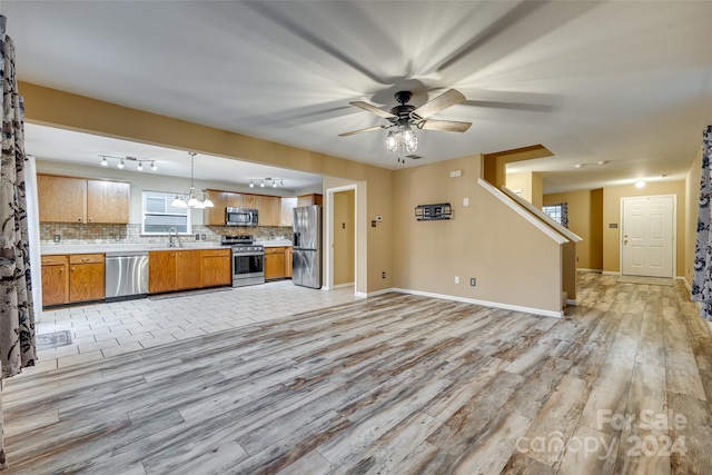 kitchen with tasteful backsplash, decorative light fixtures, appliances with stainless steel finishes, ceiling fan with notable chandelier, and light wood-type flooring