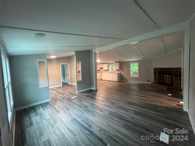 unfurnished living room featuring hardwood / wood-style floors, vaulted ceiling with beams, a stone fireplace, and sink