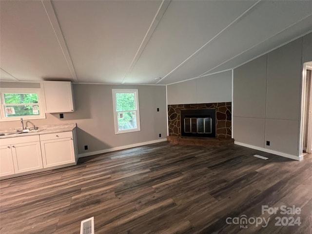 unfurnished living room with dark hardwood / wood-style flooring, a stone fireplace, sink, and lofted ceiling