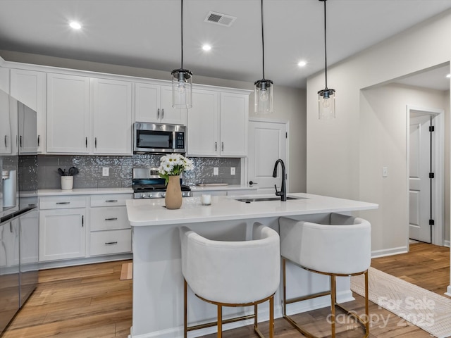 kitchen featuring appliances with stainless steel finishes, sink, a kitchen island with sink, and decorative light fixtures