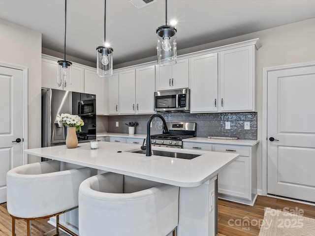 kitchen featuring pendant lighting, white cabinetry, a kitchen island with sink, and appliances with stainless steel finishes