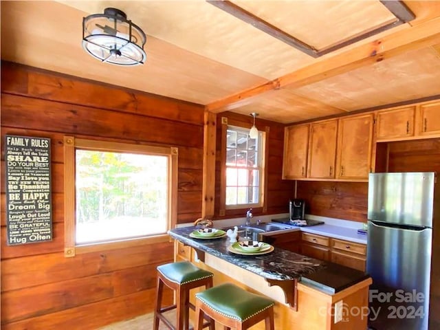 kitchen featuring wood walls, stainless steel refrigerator, sink, a kitchen breakfast bar, and hanging light fixtures