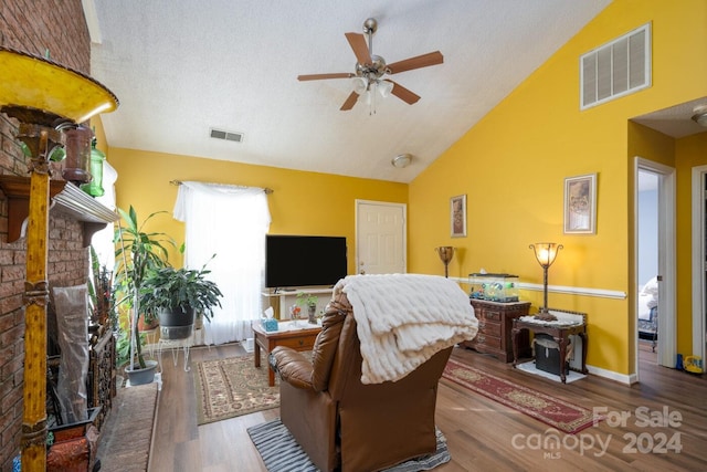 living room featuring a fireplace, hardwood / wood-style flooring, vaulted ceiling, a textured ceiling, and ceiling fan