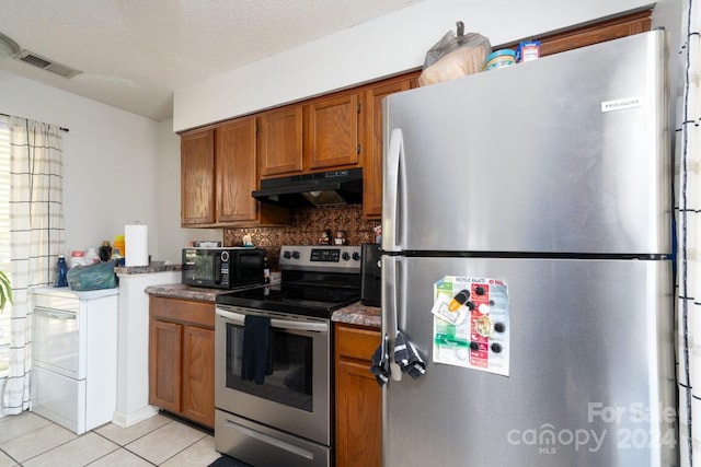 kitchen with a textured ceiling, appliances with stainless steel finishes, light tile patterned flooring, and decorative backsplash