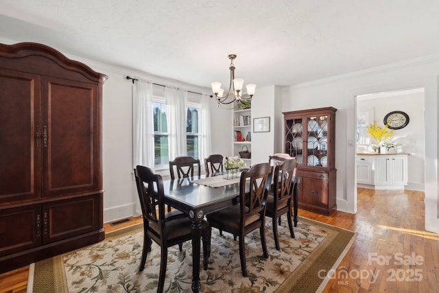 dining area with a notable chandelier, ornamental molding, and light hardwood / wood-style floors