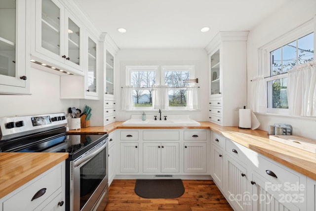 kitchen with stainless steel electric stove, a wealth of natural light, white cabinetry, sink, and butcher block countertops