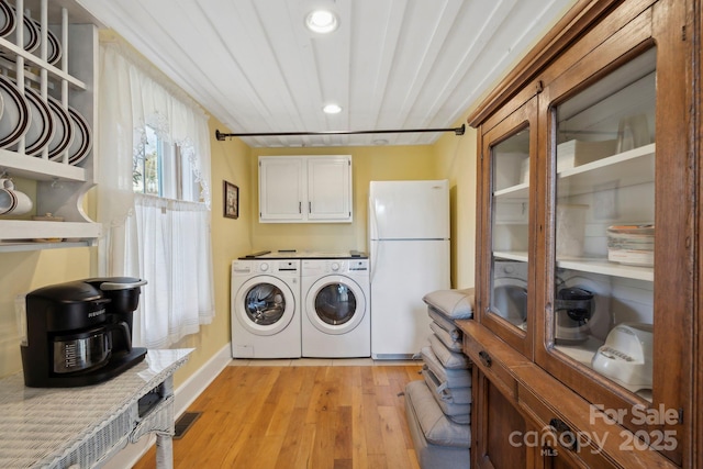 clothes washing area with washing machine and clothes dryer and light hardwood / wood-style flooring