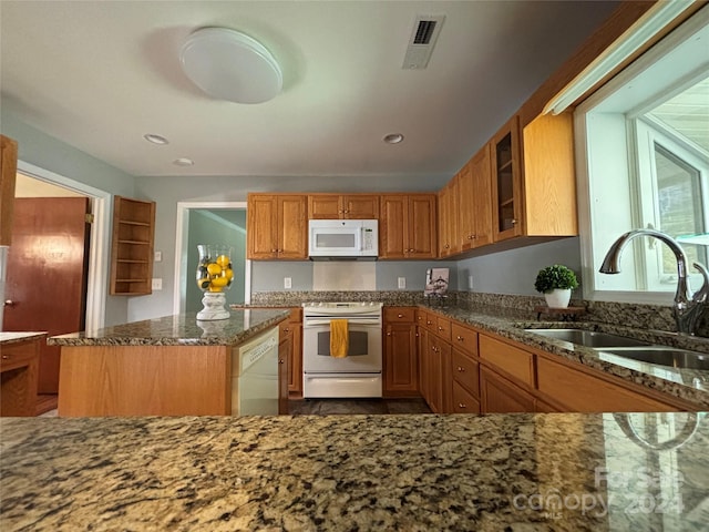 kitchen featuring white appliances, stone counters, sink, and a kitchen island