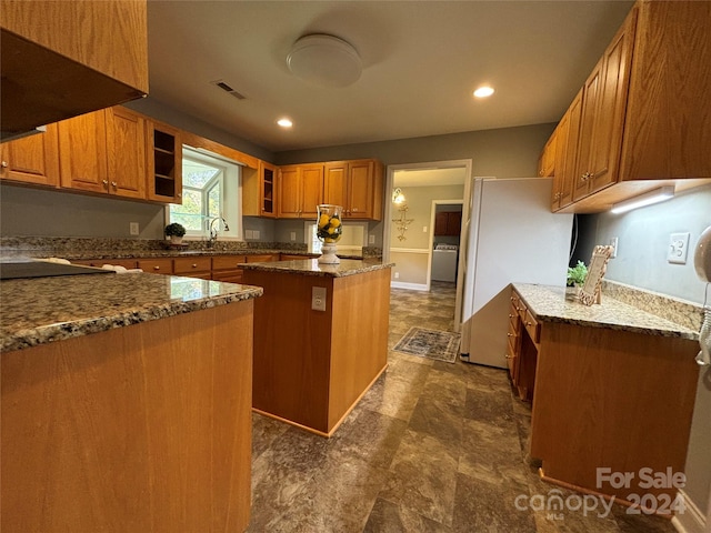 kitchen with washer / clothes dryer, extractor fan, dark stone counters, sink, and a center island