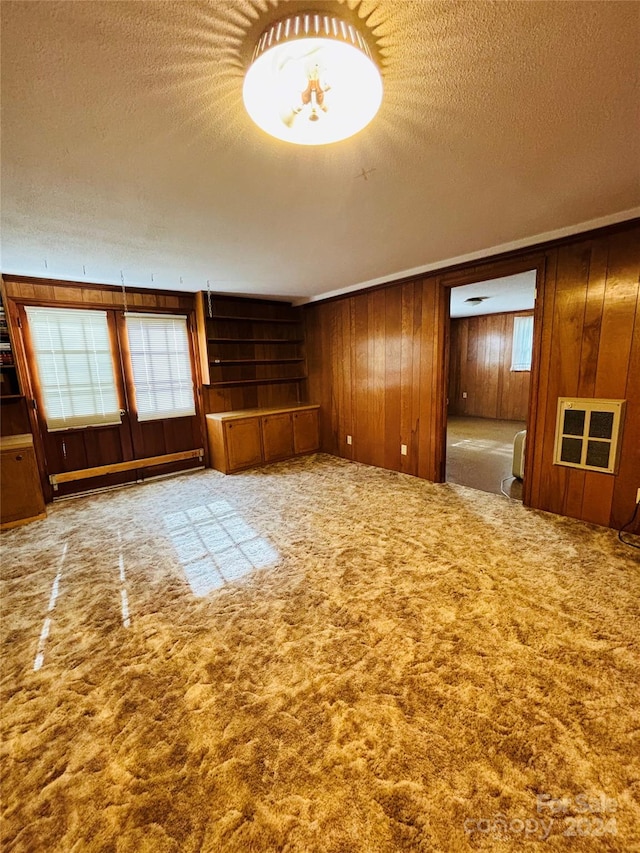 unfurnished living room with light carpet, wood walls, a healthy amount of sunlight, and a baseboard radiator