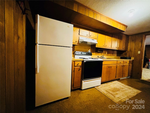 kitchen featuring dark carpet, sink, a textured ceiling, white appliances, and wood walls