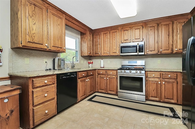 kitchen featuring black appliances, light stone counters, backsplash, light tile patterned floors, and sink