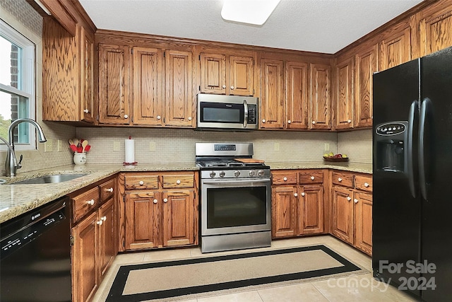 kitchen with light stone counters, black appliances, sink, light tile patterned floors, and backsplash