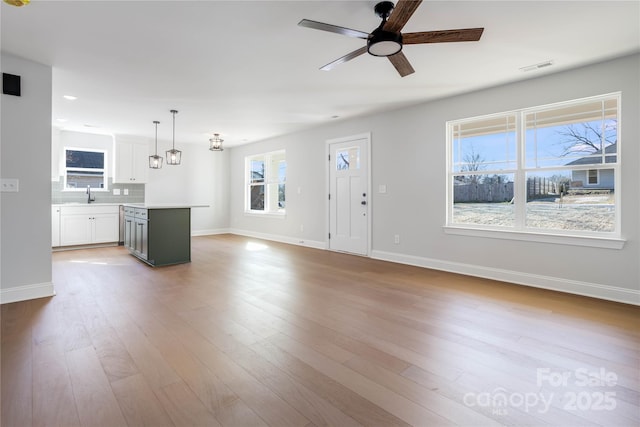 unfurnished living room with light hardwood / wood-style flooring, sink, plenty of natural light, and ceiling fan