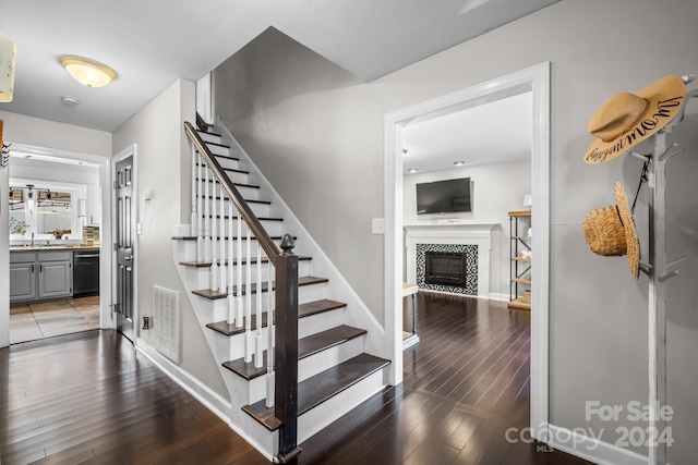 staircase with a tiled fireplace, sink, and hardwood / wood-style floors