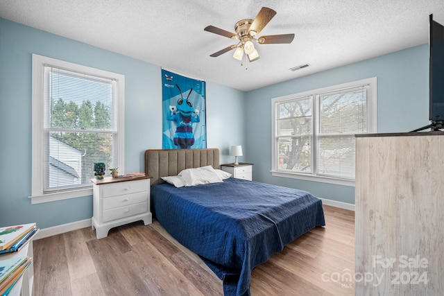 bedroom with ceiling fan, a textured ceiling, multiple windows, and light hardwood / wood-style floors