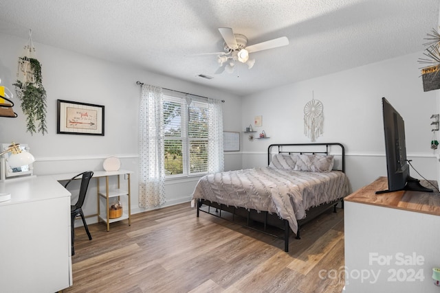 bedroom with a textured ceiling, wood-type flooring, and ceiling fan