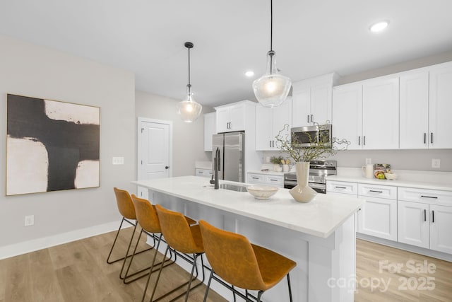 kitchen with light hardwood / wood-style flooring, pendant lighting, stainless steel appliances, a kitchen island with sink, and white cabinets