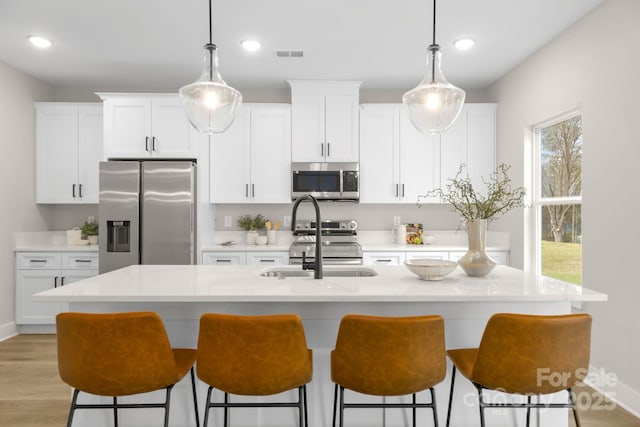 kitchen featuring white cabinetry, hanging light fixtures, stainless steel appliances, and an island with sink