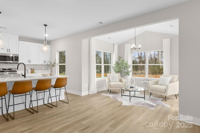 kitchen featuring appliances with stainless steel finishes, pendant lighting, white cabinets, a kitchen bar, and light hardwood / wood-style floors