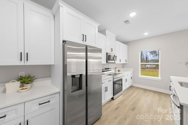 kitchen with stainless steel appliances, white cabinets, and light hardwood / wood-style flooring