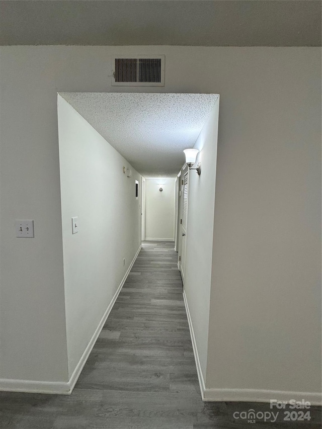 hallway with a textured ceiling and dark hardwood / wood-style floors