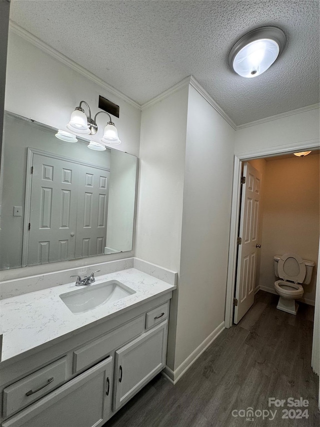 bathroom featuring wood-type flooring, a textured ceiling, toilet, vanity, and crown molding