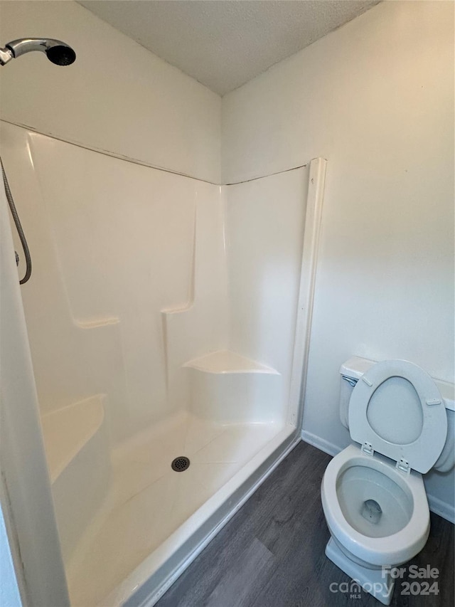 bathroom featuring toilet, a textured ceiling, wood-type flooring, and a shower