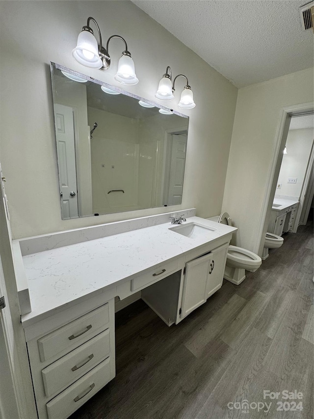 bathroom with a textured ceiling, hardwood / wood-style flooring, toilet, a bidet, and vanity