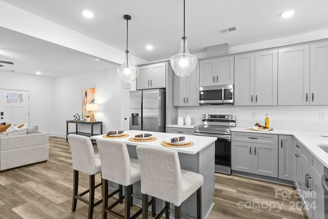 kitchen featuring stainless steel appliances, pendant lighting, gray cabinets, a kitchen island, and hardwood / wood-style flooring