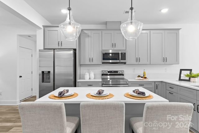 kitchen with appliances with stainless steel finishes, hardwood / wood-style flooring, gray cabinets, and hanging light fixtures