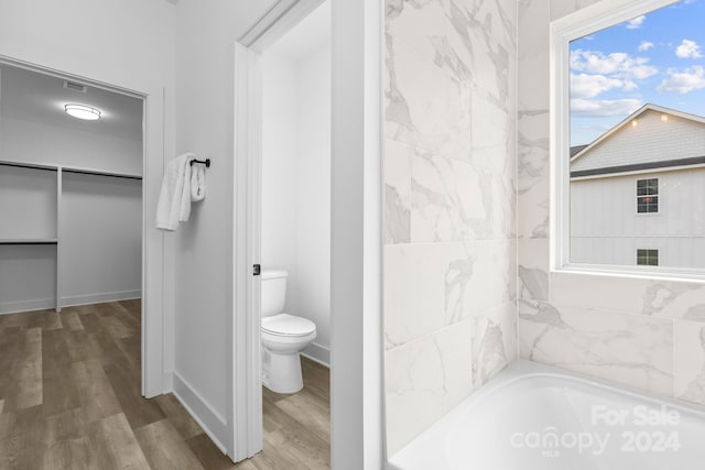 bathroom featuring hardwood / wood-style floors, a bath, and toilet