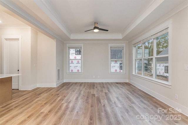 empty room featuring ceiling fan, light hardwood / wood-style floors, ornamental molding, and a raised ceiling