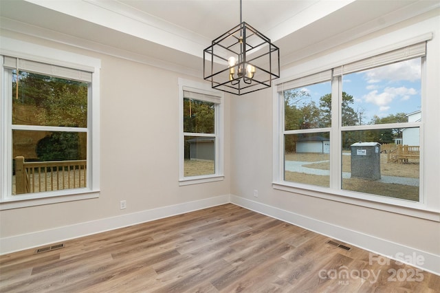 unfurnished dining area featuring plenty of natural light, a chandelier, ornamental molding, and hardwood / wood-style floors